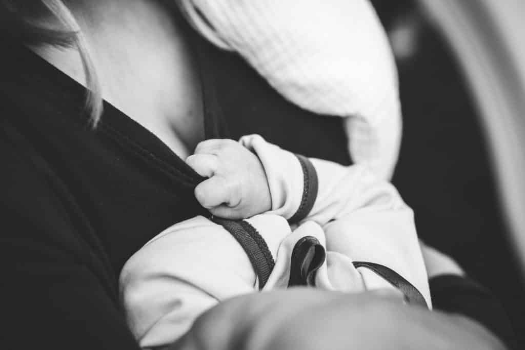 Imagem em preto e branco de uma mãe e sobre o seu colo o seu bebê. Ela está amamentando a criança.