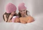 Imagem de três meninas, sendo que uma delas é uma recém nascida. As três usam uma touca rosa de lã.