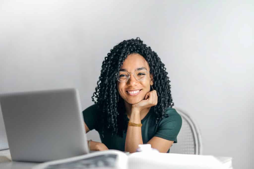 Mulher negra sorrindo com a cabeça apoiada na mão. 