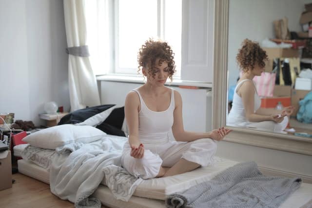 Mulher meditando em posição de lótus em colchão no chão no quarto