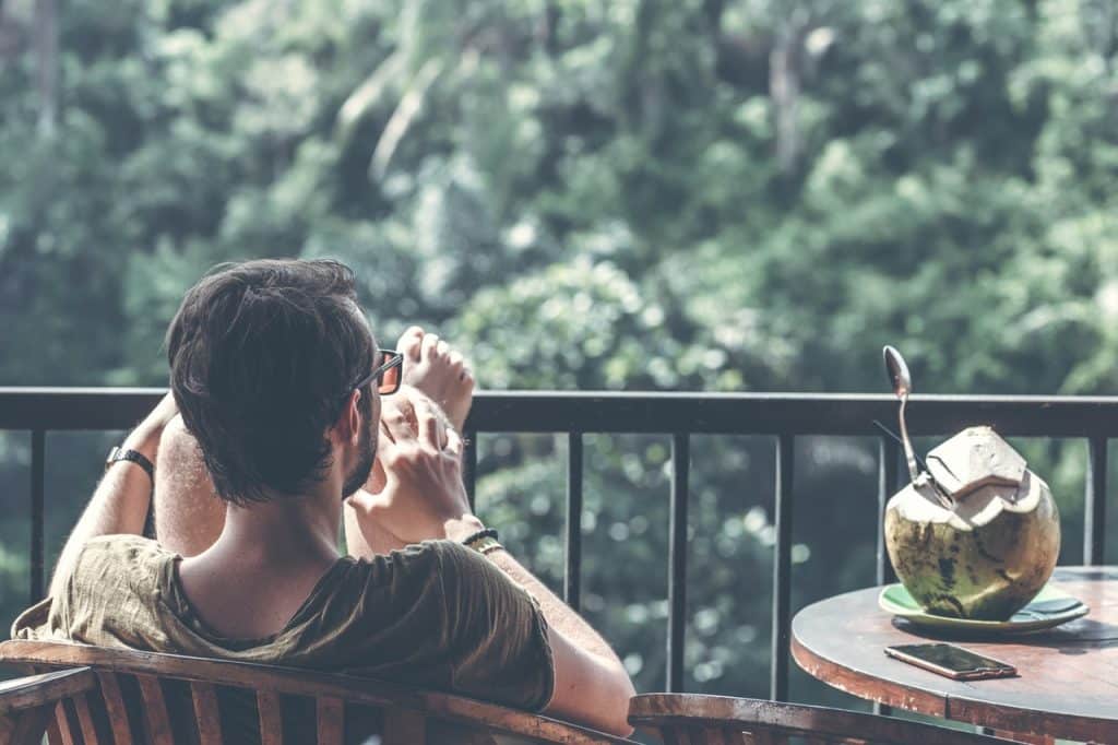 Homem sentado com as pernas para cima, ao lado de um coco com um canudo.