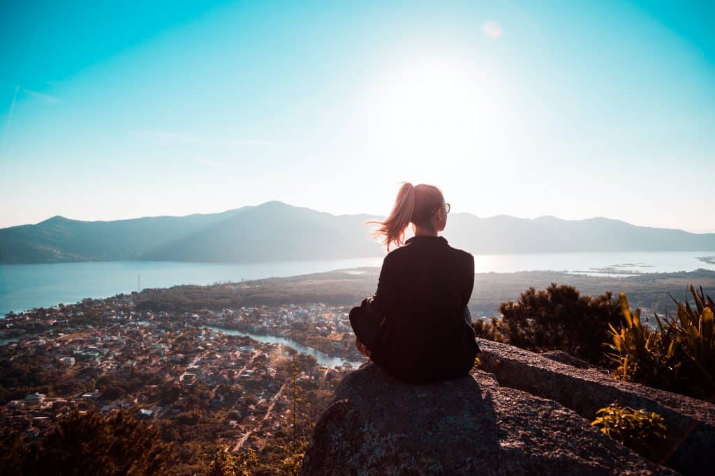 Mulher sentada em uma montanha olhando para o horizonte