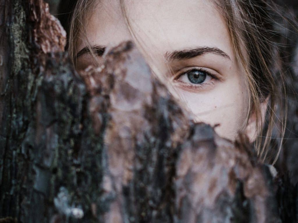 Close dos olhos de uma menina. Ela está atrás de um tronco de árvore.