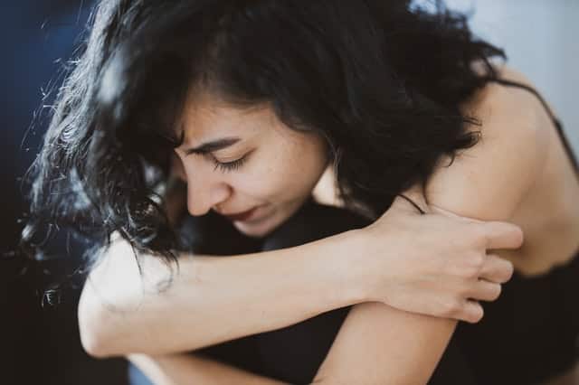 Mulher com braços em volta das pernas e expressão triste