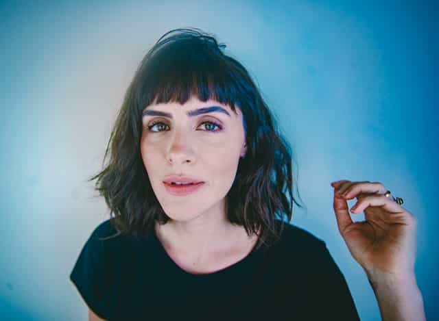 Mulher de cabelo curto e franja olhando para foto em fundo azul