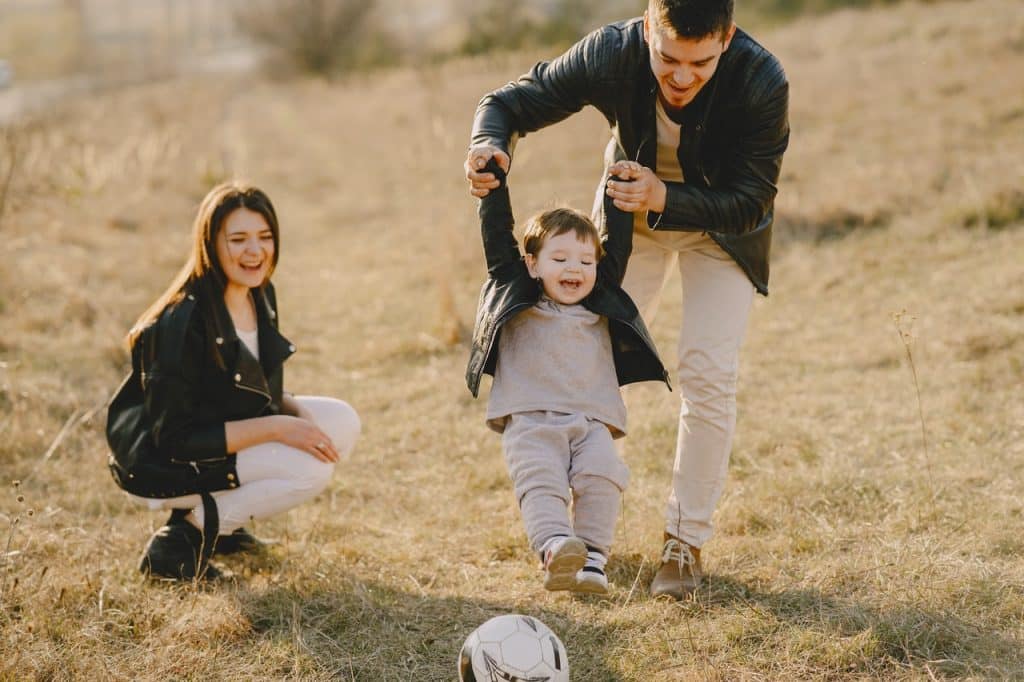 Pai, mãe e filho pequeno brincando de bola em um parque.