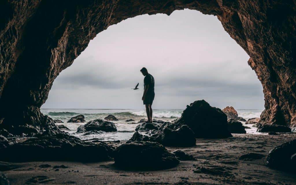 Homem numa praia em cima de uma pedra