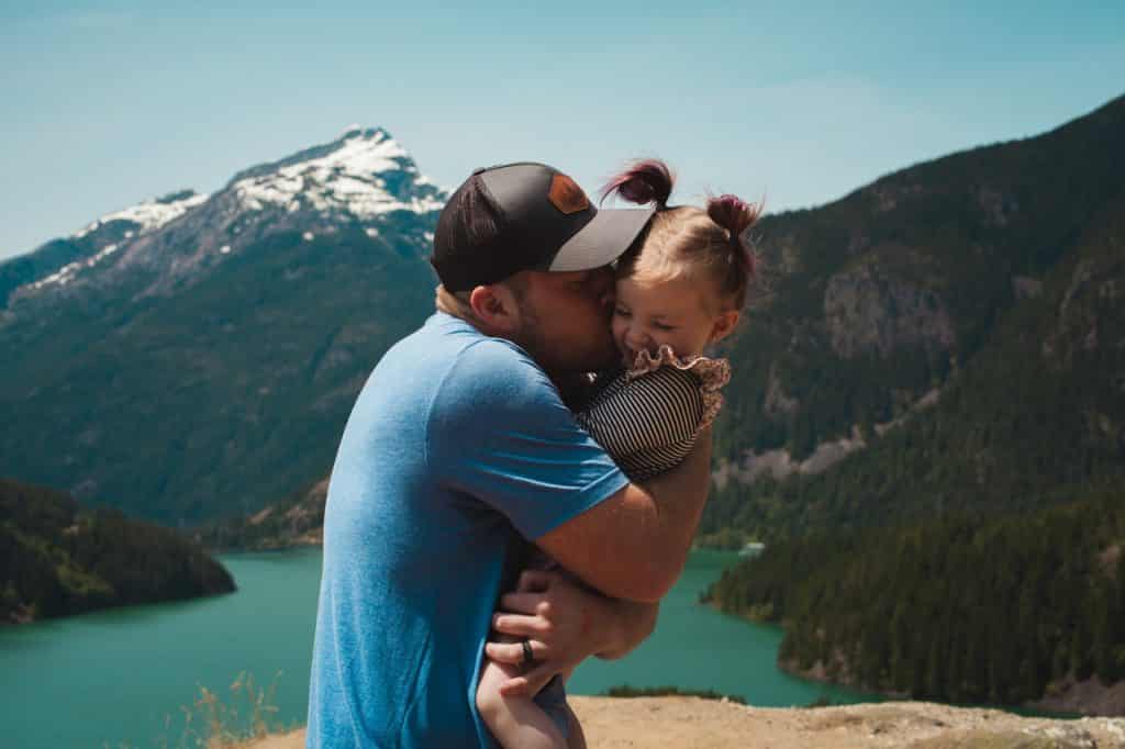 Pai abraçando e beijando a bochecha de sua filha pequena.