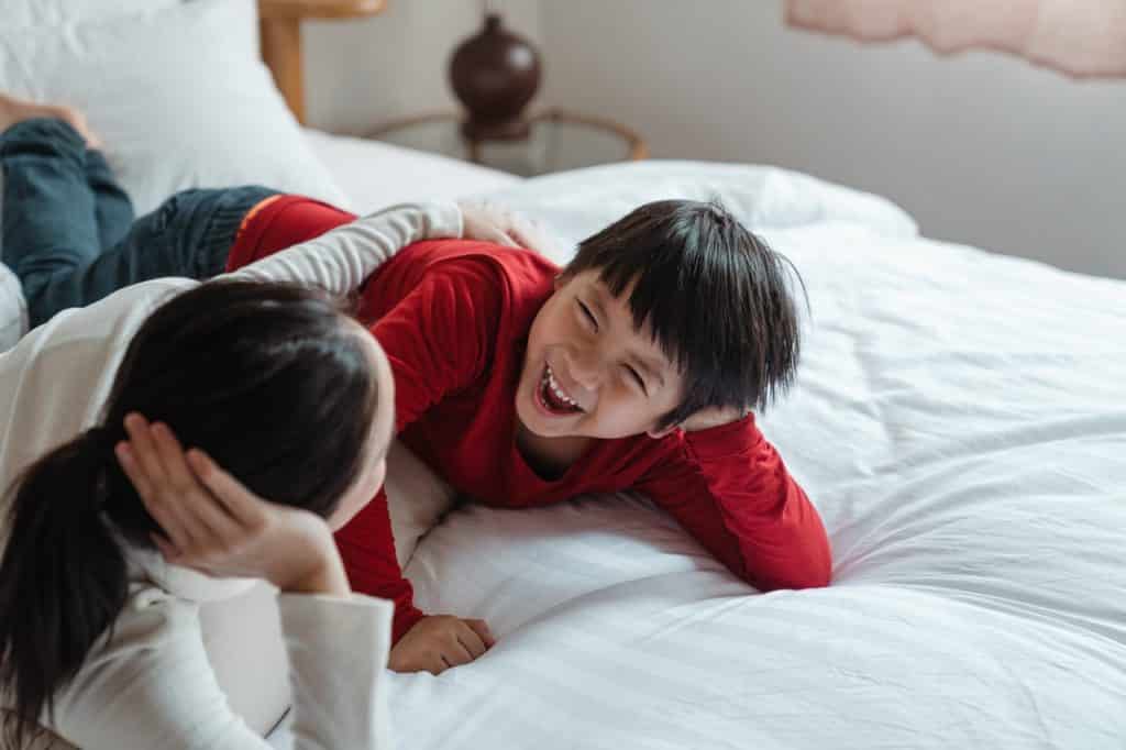 Mãe e filho conversando e rindo deitados na cama.