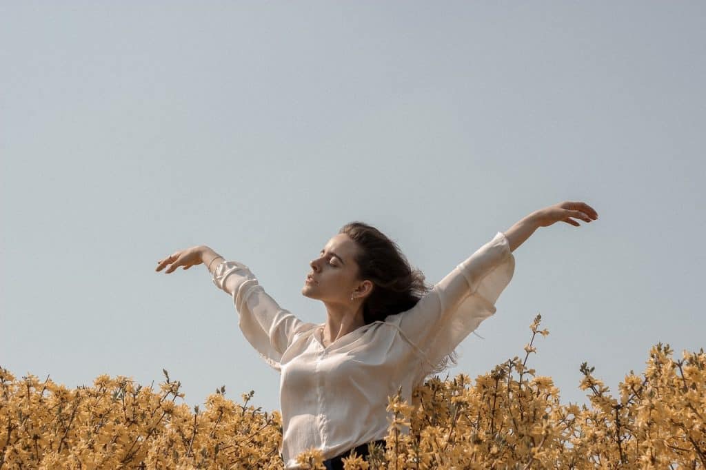 Mulher em um campo de flores, durante o dia, com as mãos para cima e os cabelos ao vento