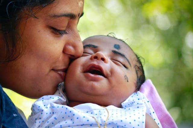 Mãe beijando rosto de filha bebê que está sorrindo 