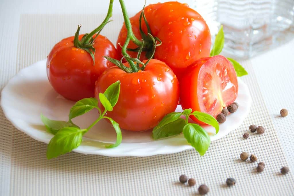 Imagem de três tomates inteiros e um pela metade dentro de um prato com algumas bolinhas de pimenta ao redor.