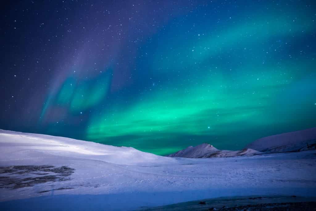 Foto de uma aurora boreal em uma montanha com neve.