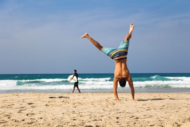 Homem fazendo estrela com mãos na areia e pernas para o alto na praia