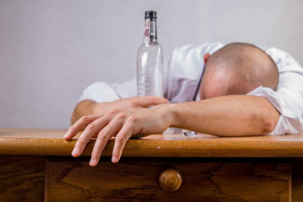 Homem debruçado sobre uma bancada abraçado a uma garrafa de bebida alcoólica.