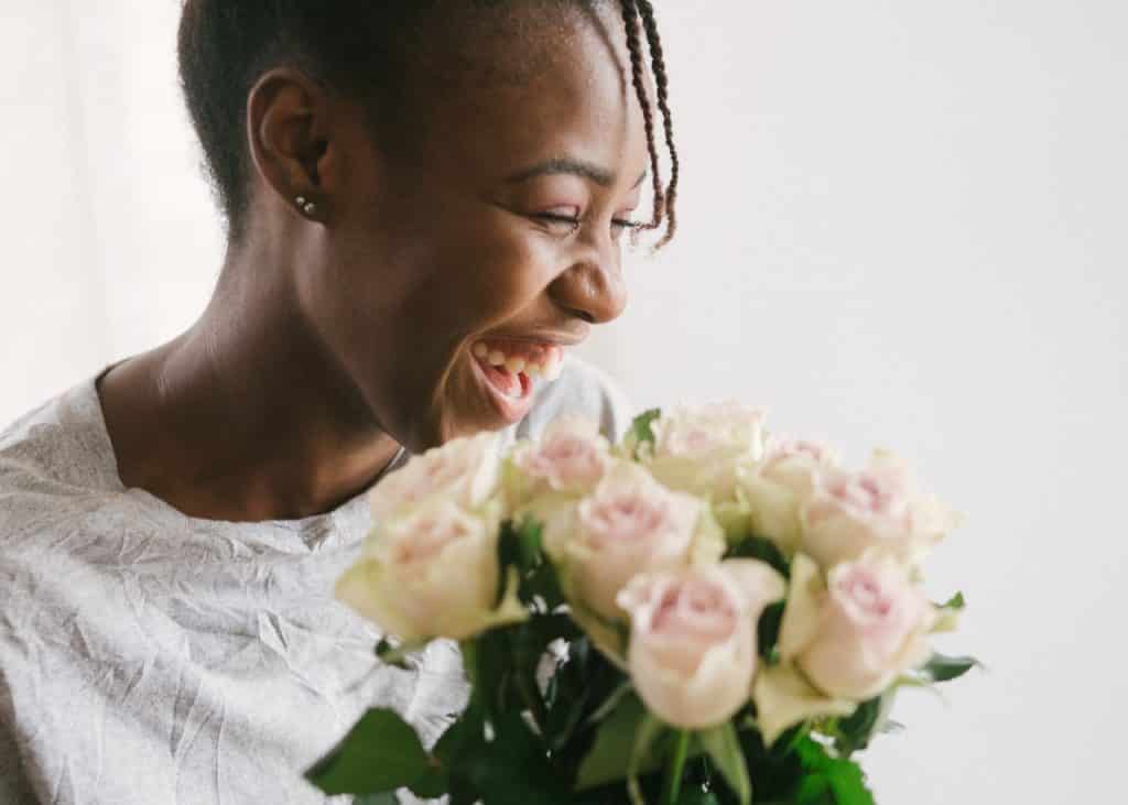 Mulher sorrindo ao segurar um buquê de flores enquanto olha para o lado,