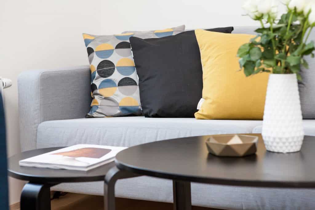 Detalhes de uma sala de estar, decorada com almofadas, plantas e mesas de centro.