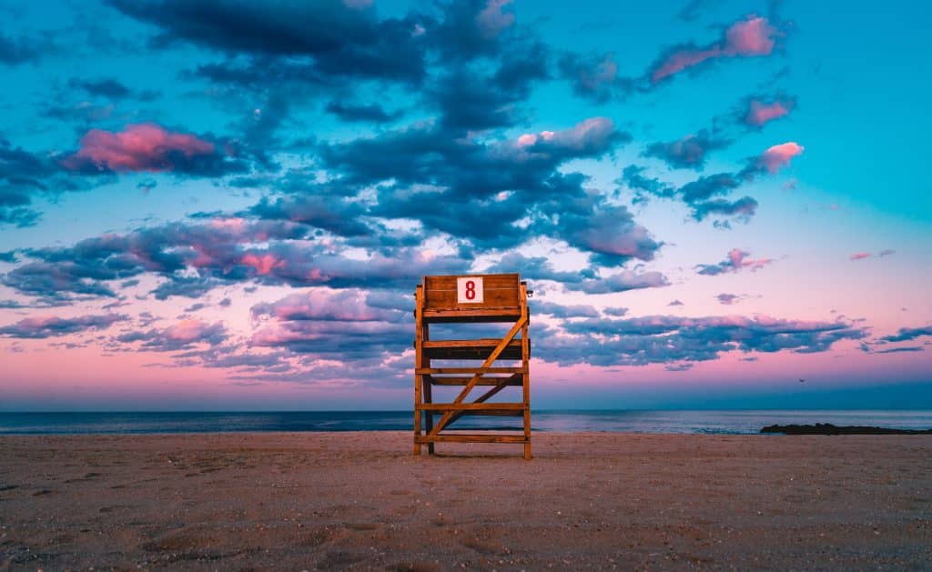 Pedestal de madeira com o número "8" na praia, pôr-do-sol ao fundo.