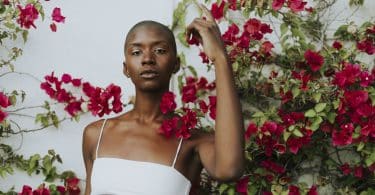 Mulher negra com top branco meio a uma árvore com flores vermelhas