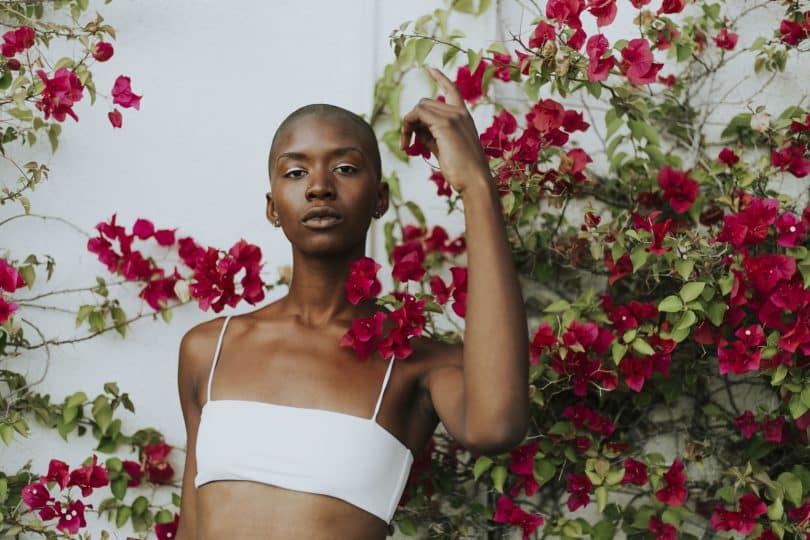 Mulher negra com top branco meio a uma árvore com flores vermelhas