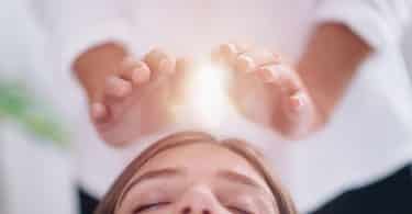 Mulher deitada de olhos fechados recebendo tratamento do Reiki