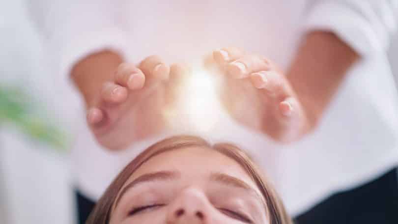 Mulher deitada de olhos fechados recebendo tratamento do Reiki