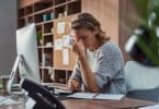 Mulher estressada em ambiente de trabalho, com os dedos sobre a testa.