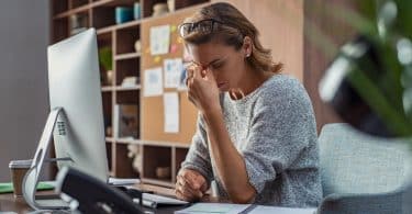 Mulher estressada em ambiente de trabalho, com os dedos sobre a testa.