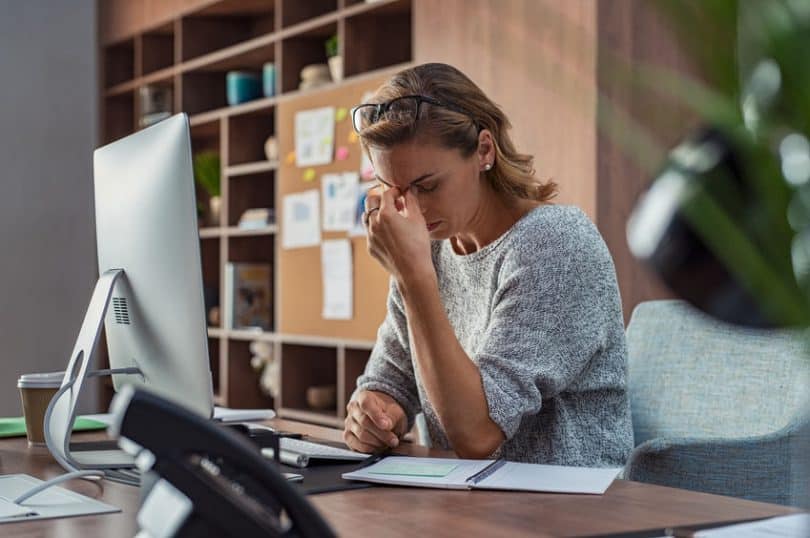 Mulher estressada em ambiente de trabalho, com os dedos sobre a testa.