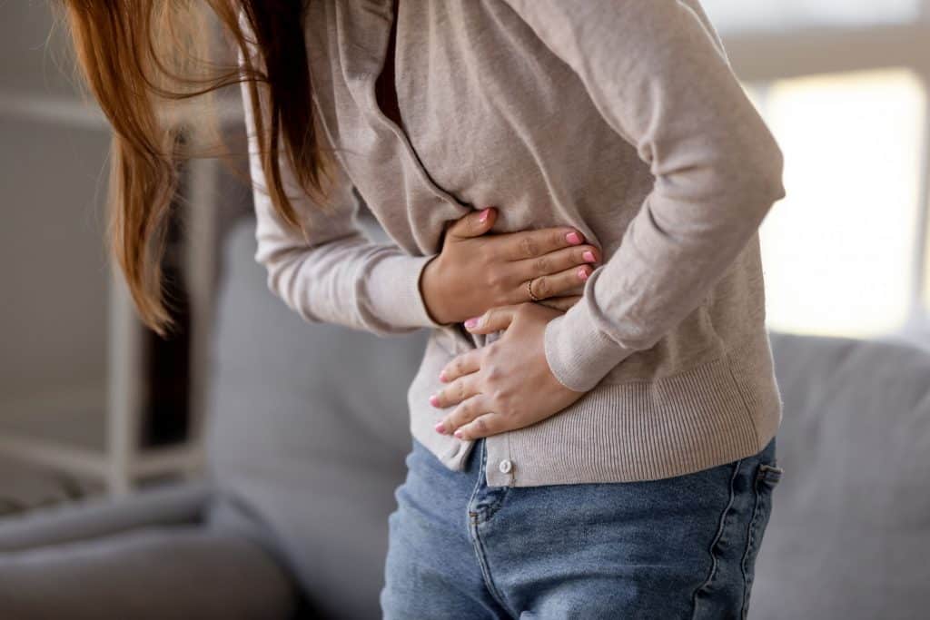 Mulher com as mãos na barriga sentindo dor