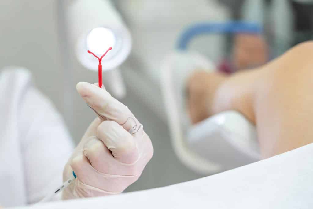 Doutora segurando DIU ao lado da paciente