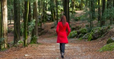 Mulher usando casaco vermelho caminhando numa floresta.