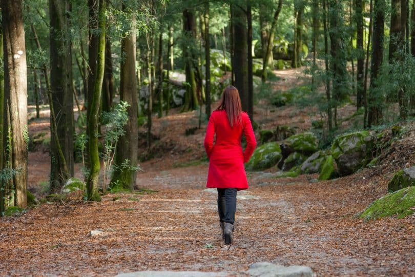 Mulher usando casaco vermelho caminhando numa floresta.