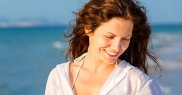 Mulher na praia sorrindo olhando para baixo com vento no cabelos