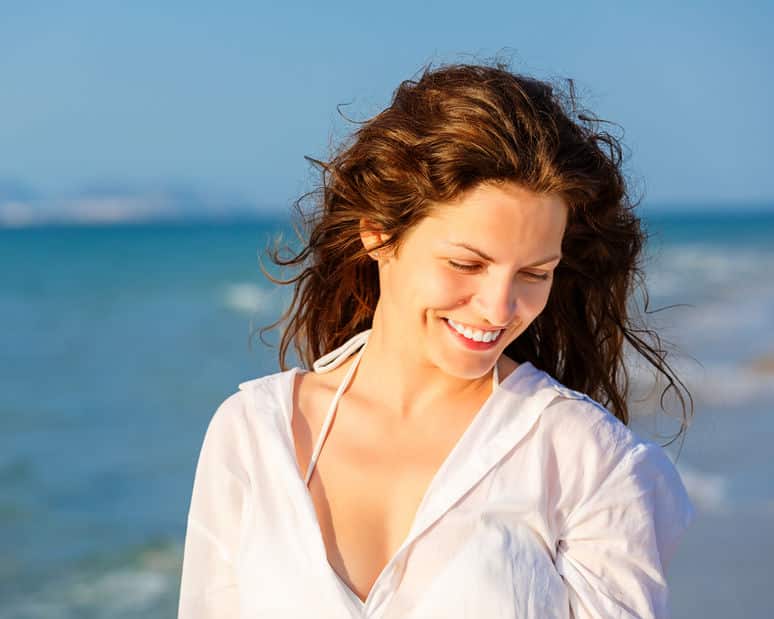 Mulher na praia sorrindo olhando para baixo com vento no cabelos