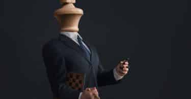 Corpo masculino com peça de xadrez no lugar da cabeça e segurando outros peças nas mãos.