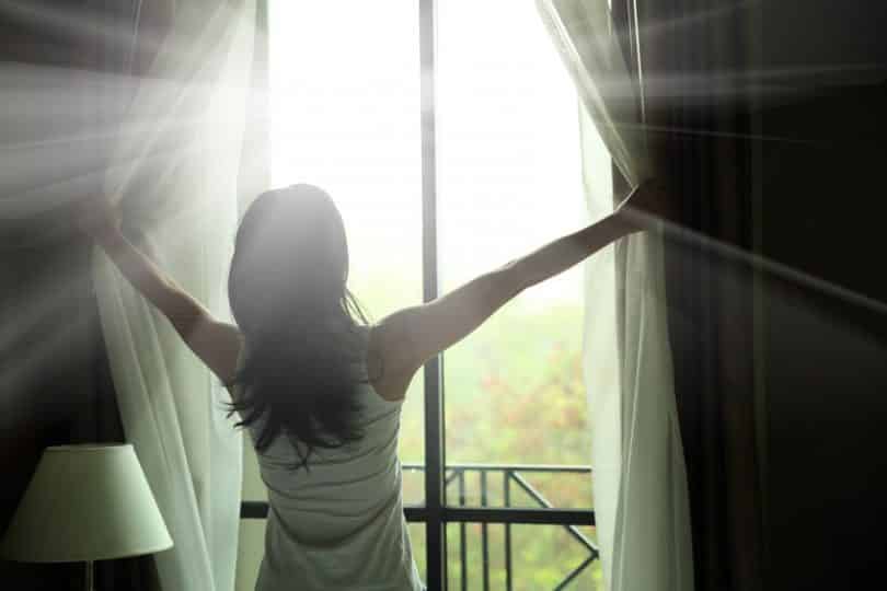 Mulher abrindo a janela com luz refletindo