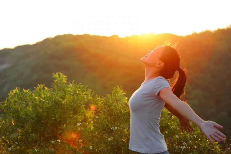 Mulher vista de perfil em um parque, com os braços abertos, sorrindo.