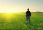 Homem em pé de costas em campo ver com sol se pondo ao fundo