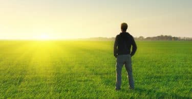 Homem em pé de costas em campo ver com sol se pondo ao fundo