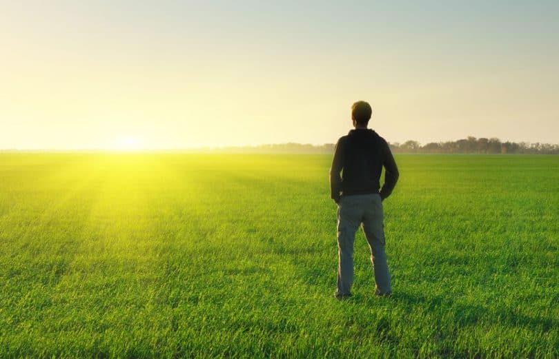 Homem em pé de costas em campo ver com sol se pondo ao fundo