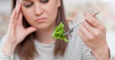 Mulher com expressão triste comendo salada