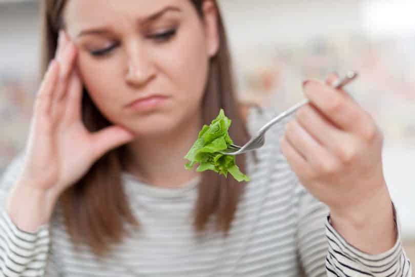 Mulher com expressão triste comendo salada