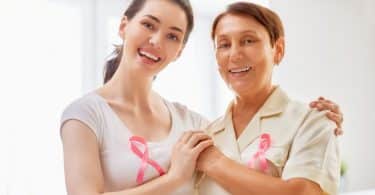 Mãe e filha abraçadas sorrindo com laço rosa no peito