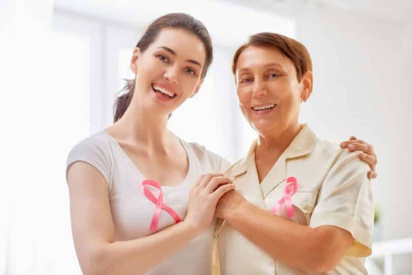 Mãe e filha abraçadas sorrindo com laço rosa no peito