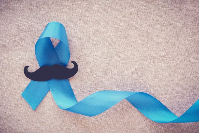 Fita azul com o símbolo do Novembro Azul e um bigode preto de papel em cima.