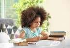 Menina na mesa de casa estudando com livros ao lado