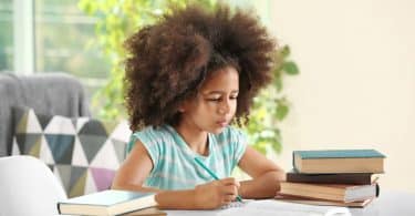 Menina na mesa de casa estudando com livros ao lado