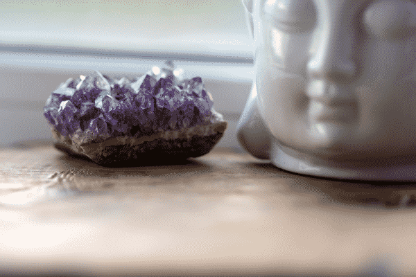Pedra ametista em mesa com imagem de buda de porcelana ao lado