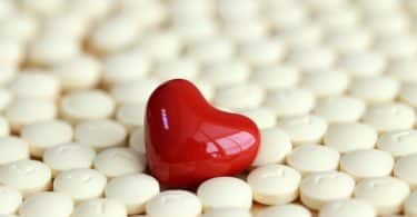 Imagem de várias pílulas contraceptivas na cor branca. Ao centro dela, uma pílula em formato de coração na cor vermelha.